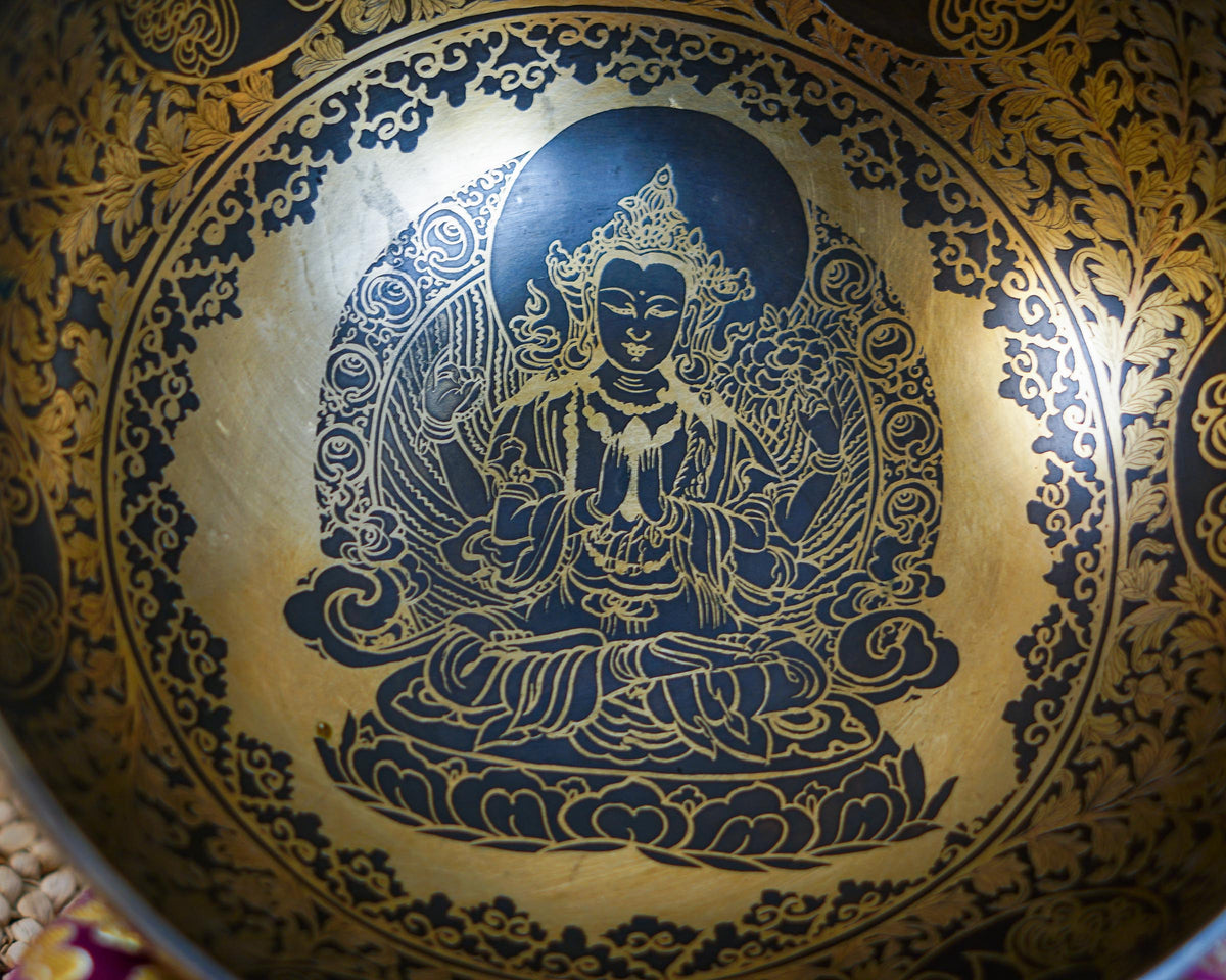 Close up of Chengresi seated on a lotus throne engraved inside a golden Tibetan singing bowl with intricate floral patterns.
