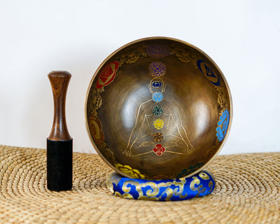 Top-angled view of a 7 chakra meditating yogi Tibetan singing bowl on a blue cushion next to a wooden striker mallet.