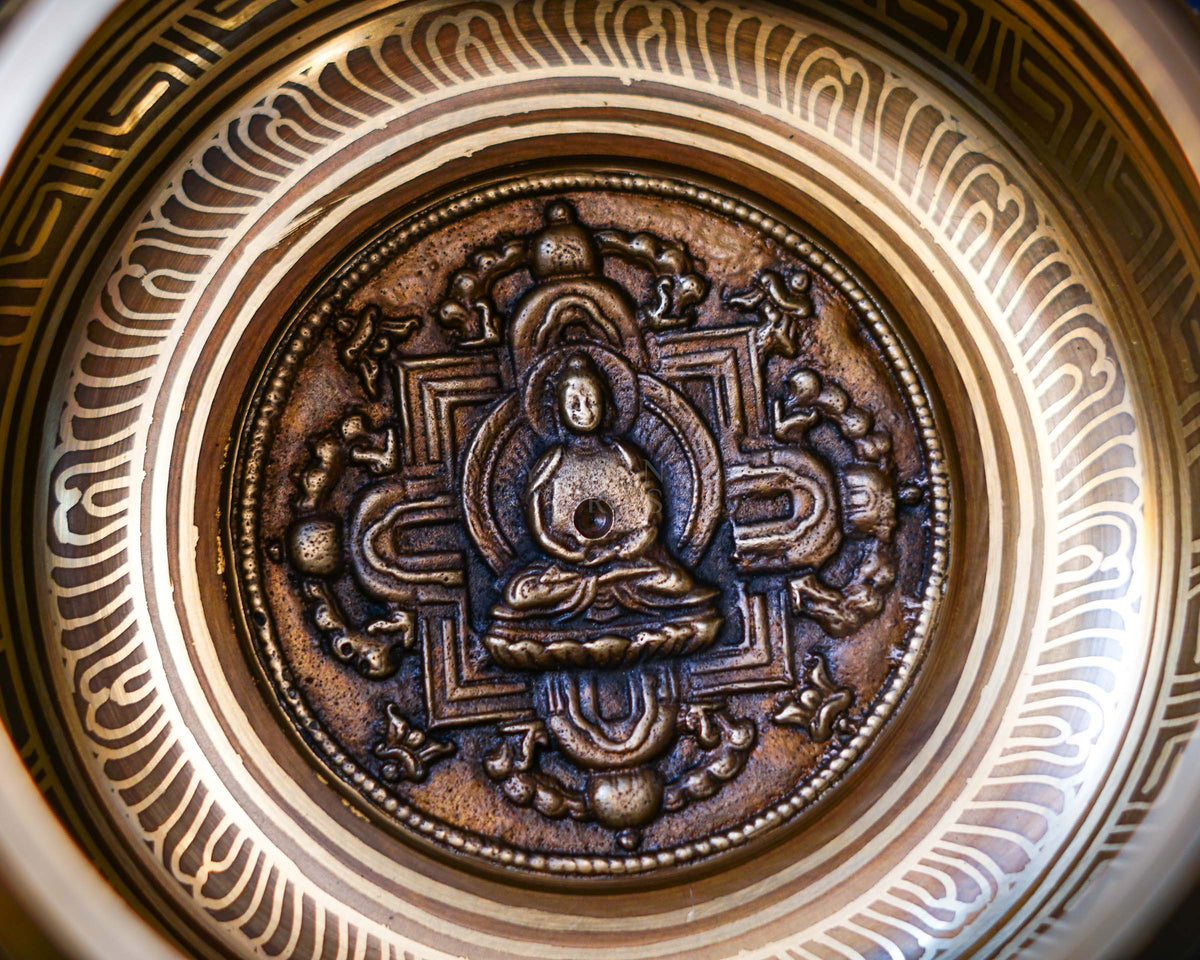 Close-up of raised Buddha relief and mandala-inspired engraving inside bronze singing bowl