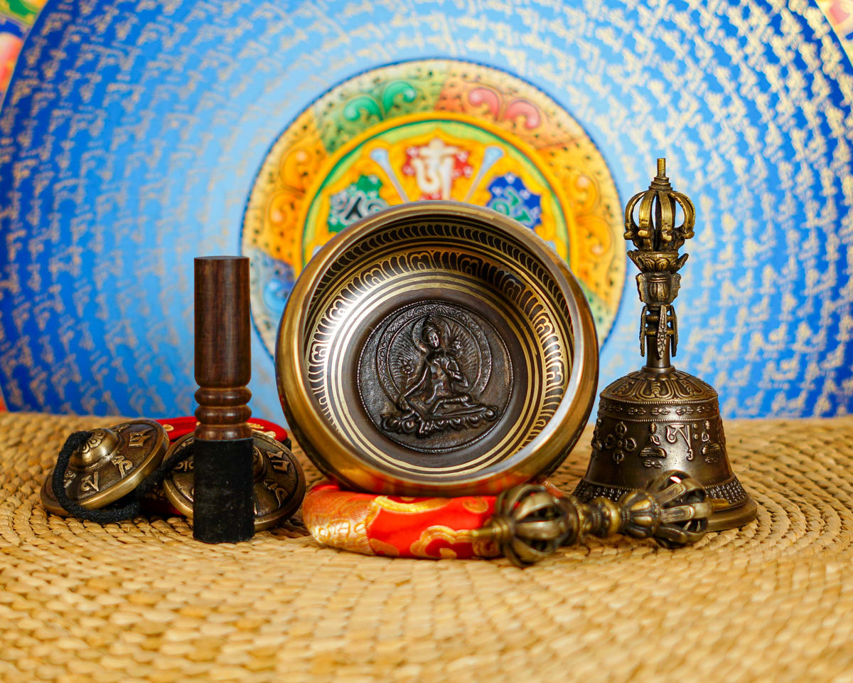 Green Tara bronze singing bowl displayed with traditional Buddhist bell and vajra