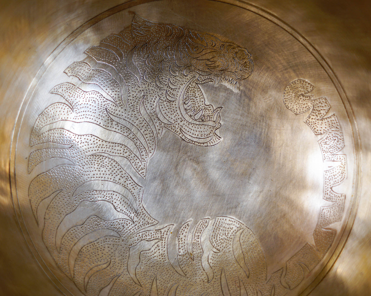 Close up of a detailed hand-engraved tiger motif with fine stippling inside a golden bronze Tibetan singing bowl.