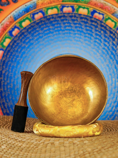 Mahakala Tibetan singing bowl with engraved deity design and yellow cushion