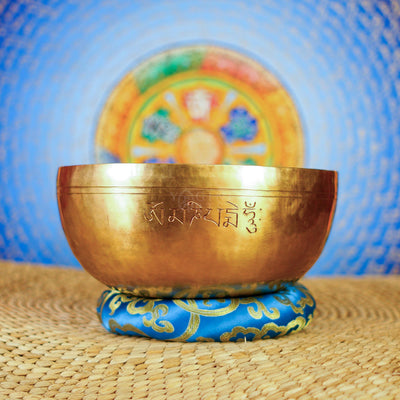 Handcrafted Tibetan singing bowl with engraved lotus flower design on the interior and blue decorative cushion