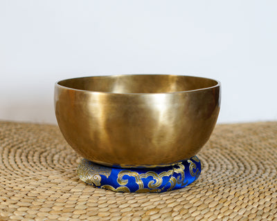 Side view of a classic plain hand-hammered bronze Tibetan singing bowl resting on a blue brocade cushion.