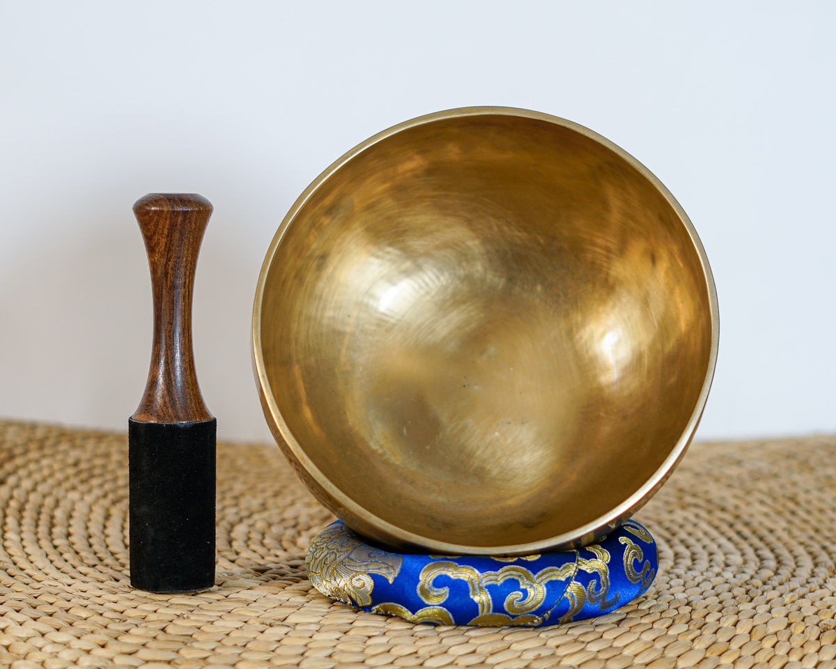 Side view of a classic plain hand-hammered bronze Tibetan singing bowl resting on a blue brocade cushion.