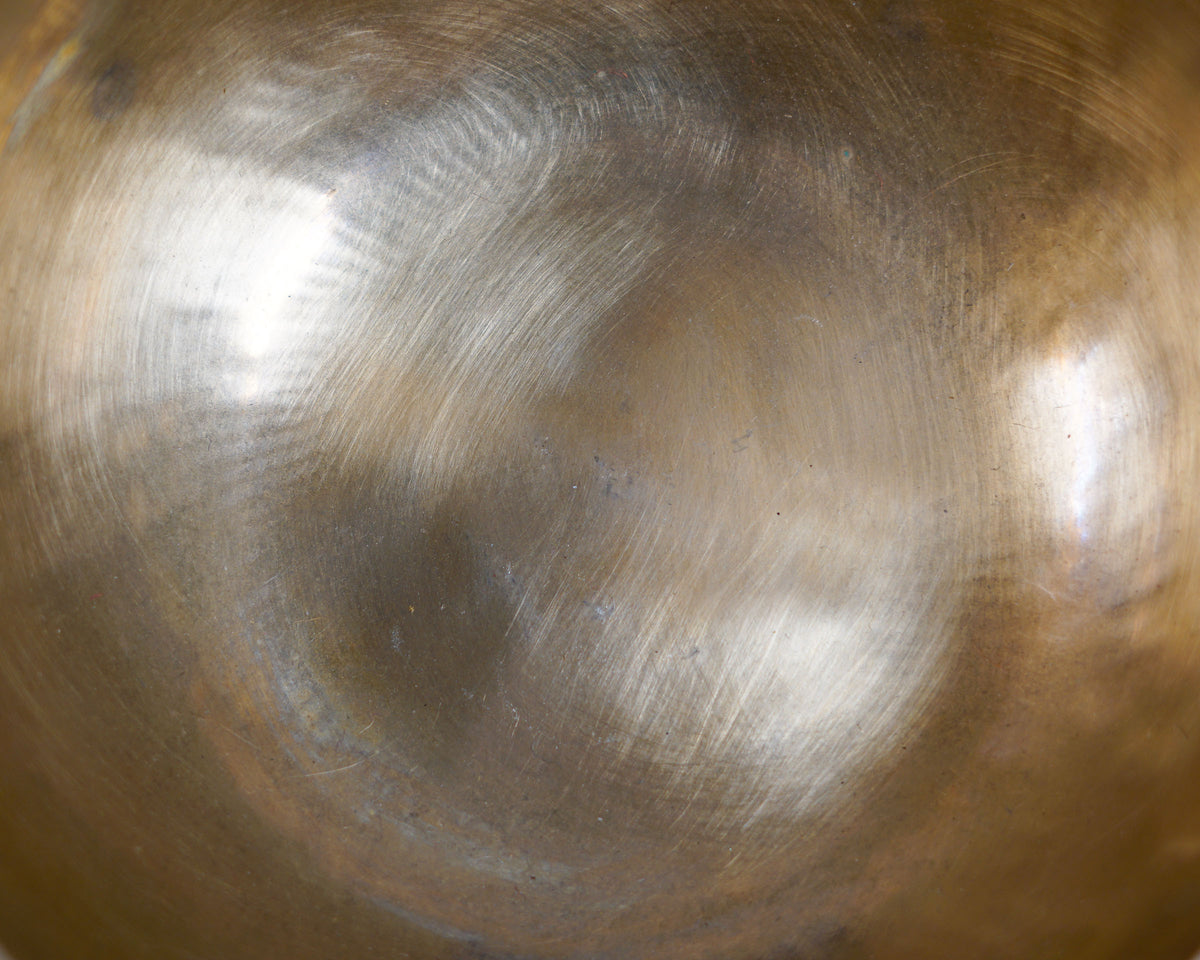 Side view of a classic plain hand-hammered bronze Tibetan singing bowl resting on a blue brocade cushion.