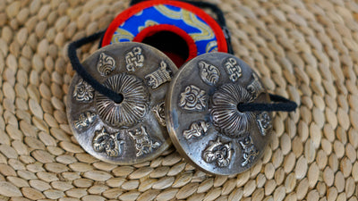 Close up of Tibetan tingsha cymbals engraved with eight auspicious Buddhist symbols and a black connecting cord.