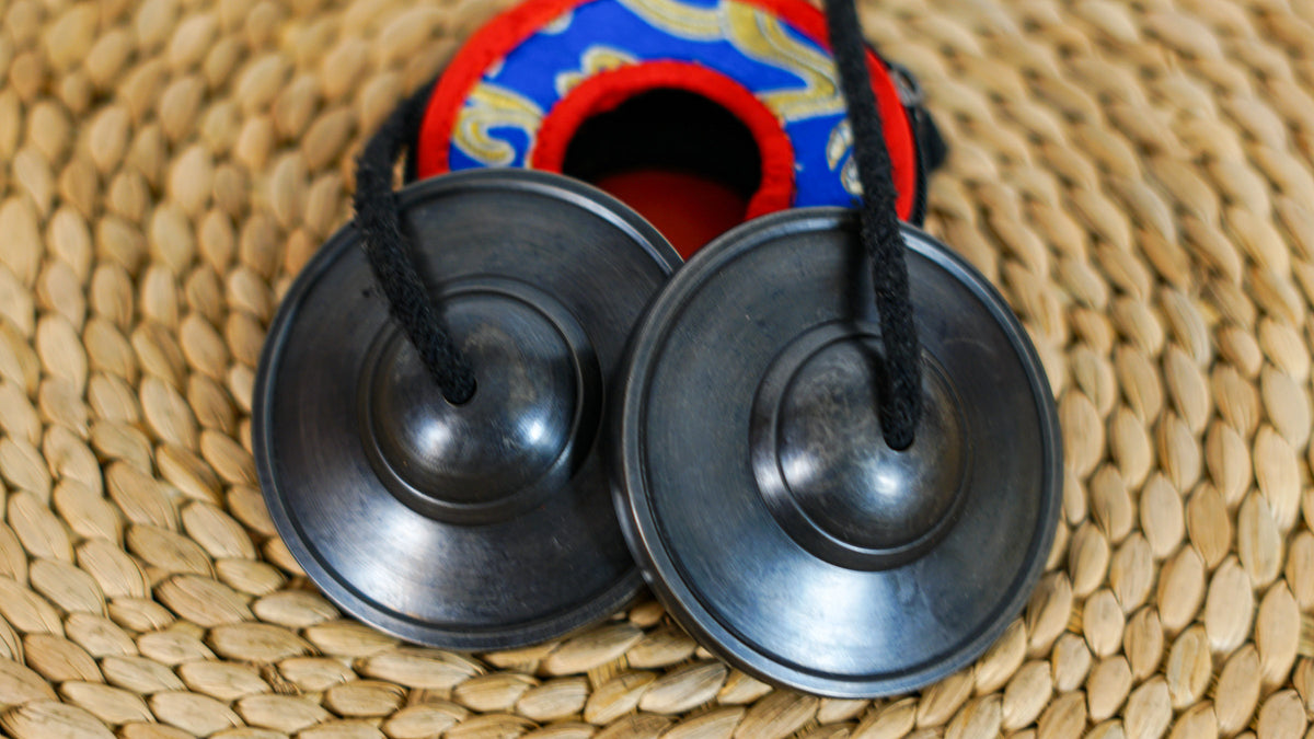 Close up of black Tibetan meditation cymbals showing their smooth circular surfaces and raised central details.