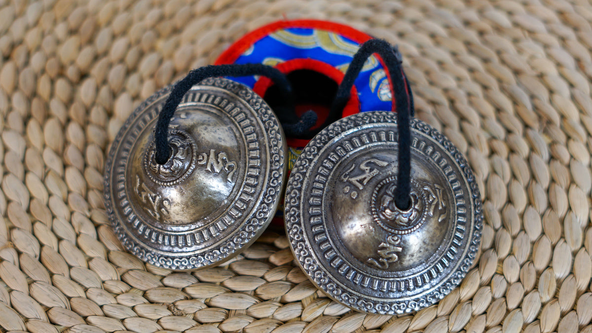 Pair of Tibetan meditation cymbals with an antique metallic finish displayed with a colorful brocade case.