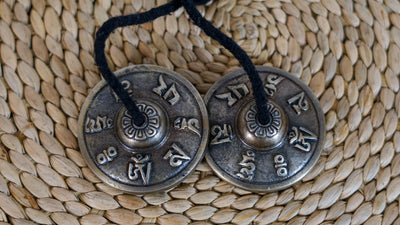 Angled view of Tibetan Mantra Tingsha Cymbals with textured metal surfaces and decorative raised engravings.