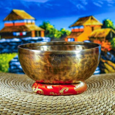 Side view of a handcrafted Himalayan singing bowl with warm bronze-gold finish, engraved Tibetan-style inscription and red decorative cushion.