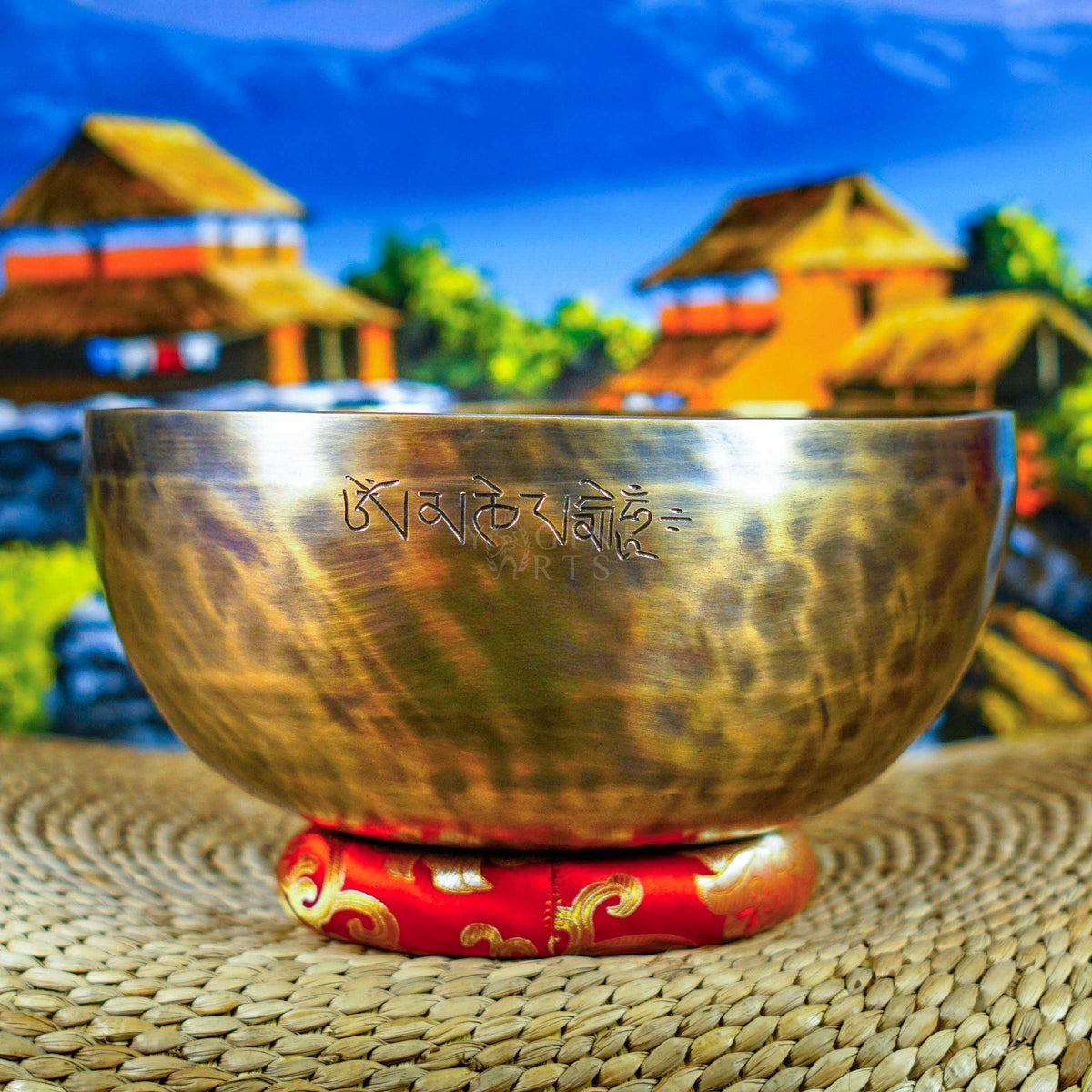 Side view of a handcrafted Himalayan singing bowl with warm bronze-gold finish, engraved Tibetan-style inscription and red decorative cushion.