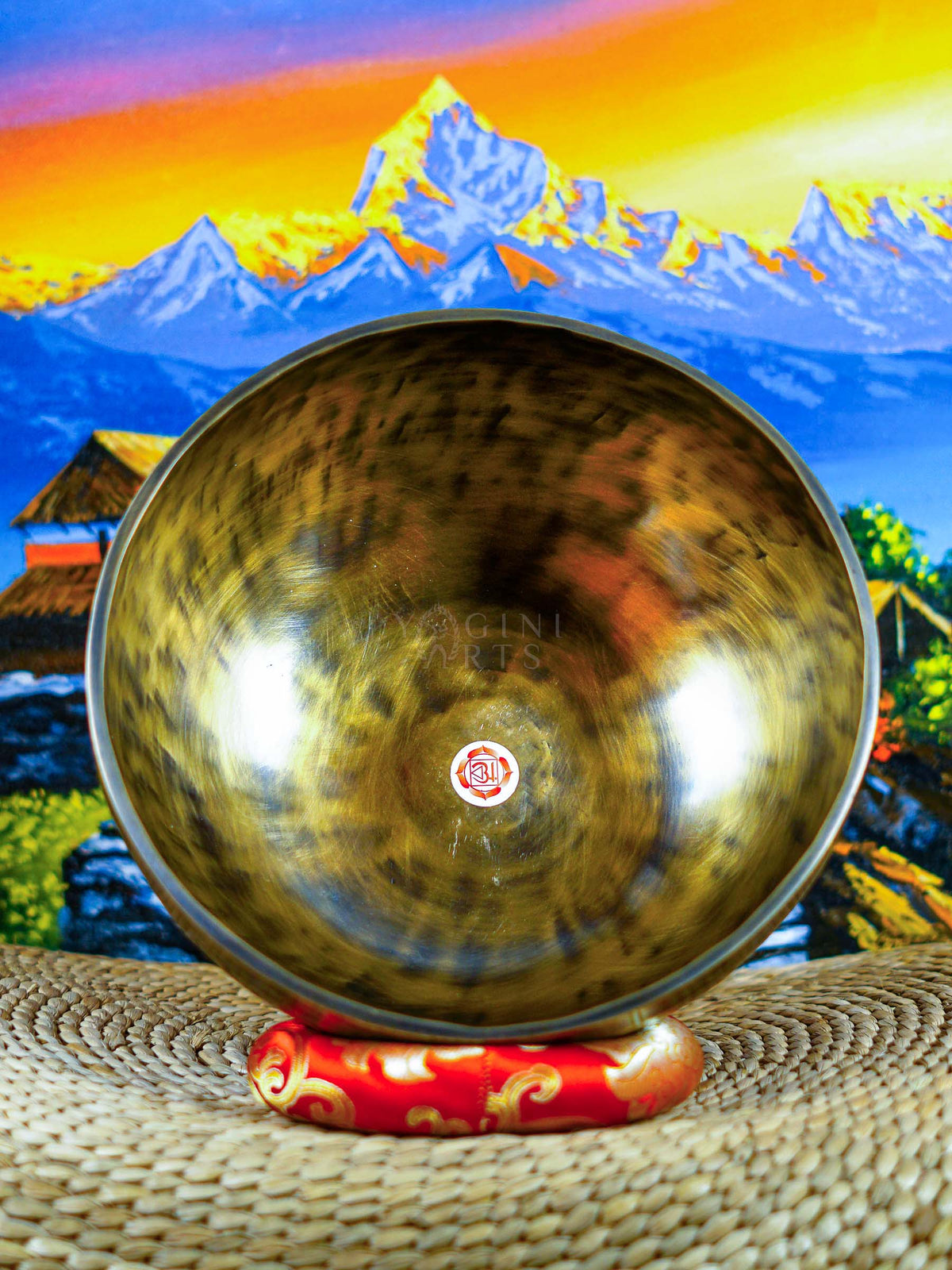 Front view of a chakra singing bowl displaying the Om symbol inside a warm bronze-gold metal bowl on a red cushion.