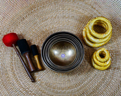 Seven handcrafted Himalayan singing bowls arranged together, featuring graduated sizes, chakra symbols, and warm antique bronze-gold finishes.