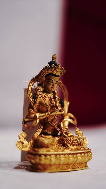 Golden statue of a seated Buddhist deity with intricate detailing, displayed on a plain background.