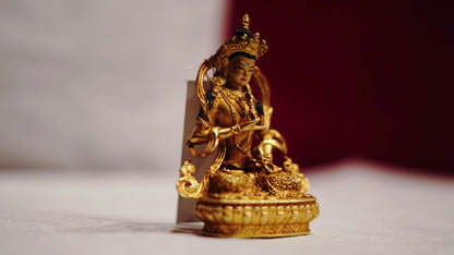 Golden statue of a seated Buddhist deity with intricate detailing, displayed on a plain background.