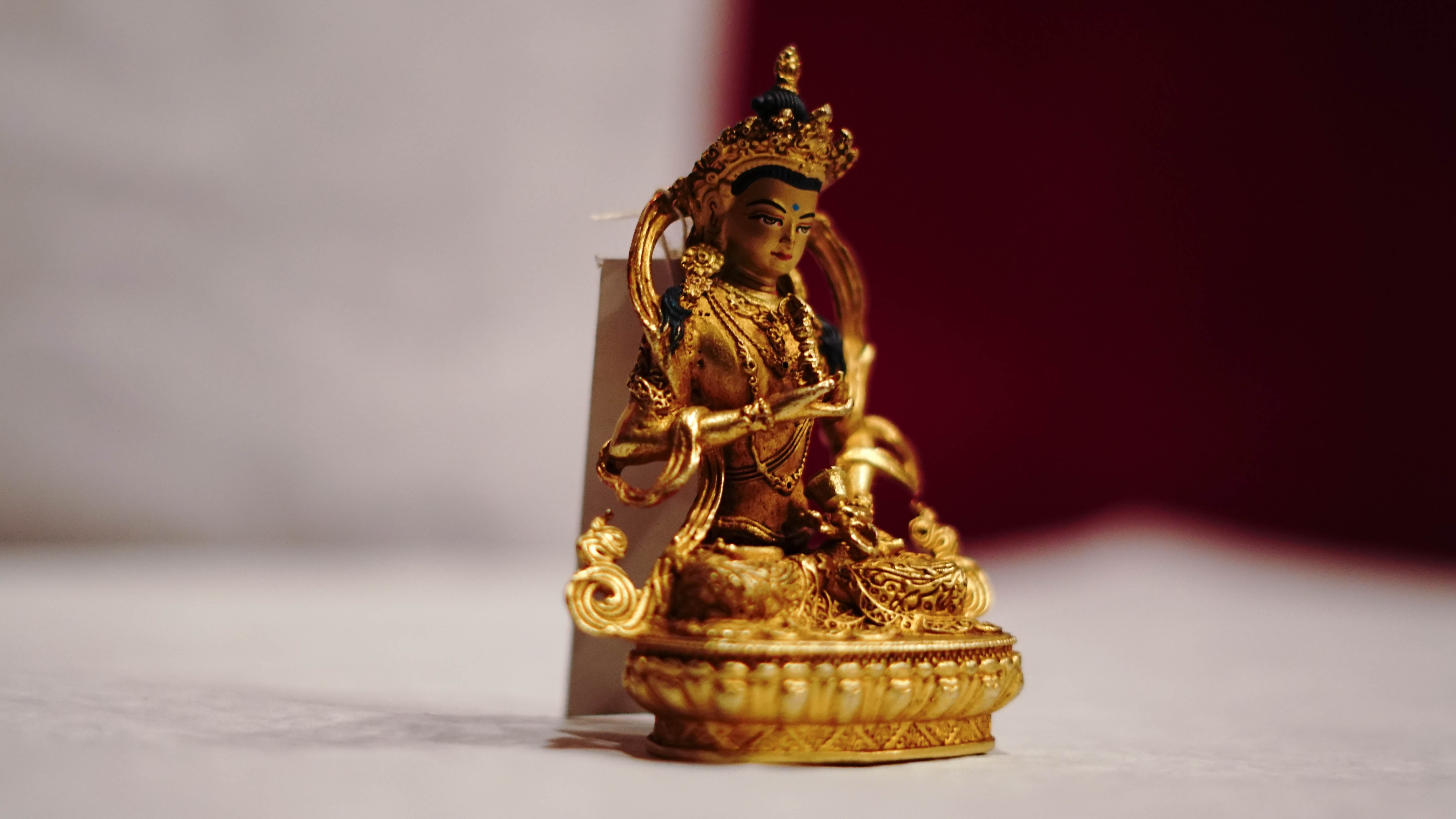 Golden statue of a seated Buddhist deity with intricate detailing, displayed on a plain background.