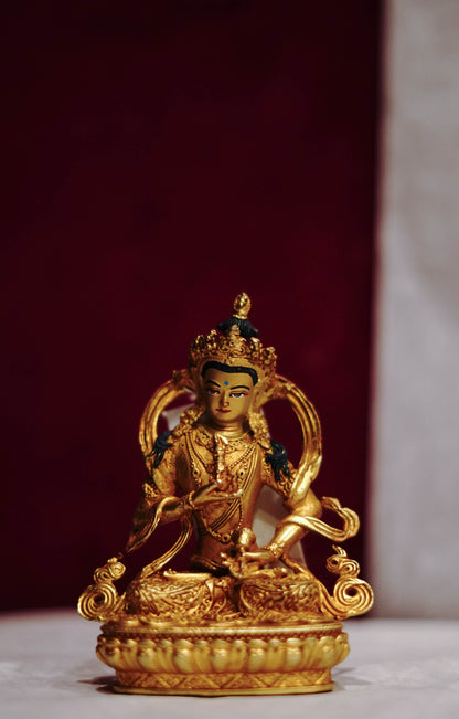 Golden statue of a seated Buddhist deity with intricate detailing, displayed on a plain background.