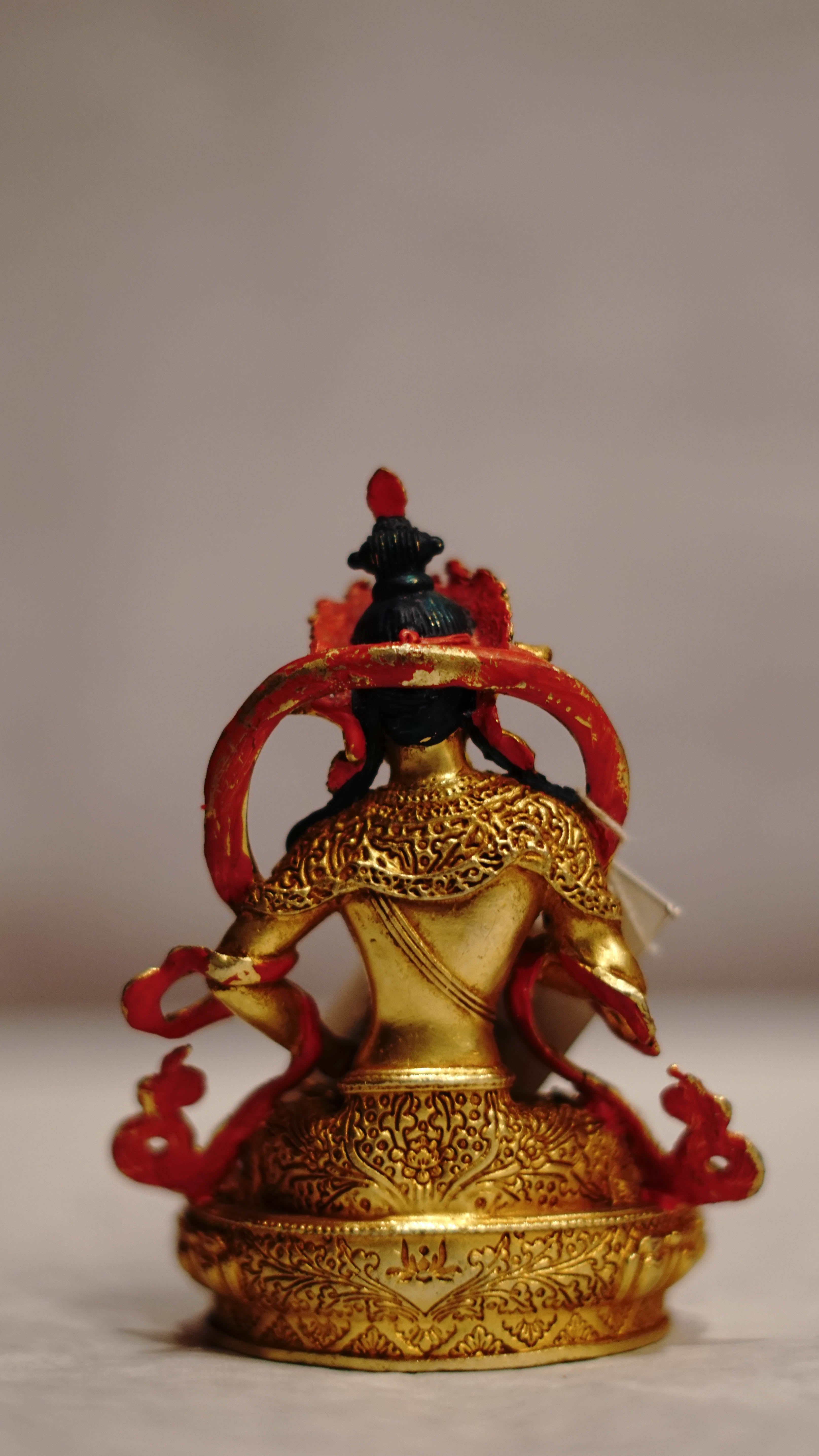 Golden statue of a seated Buddhist deity with intricate detailing, displayed on a plain background.