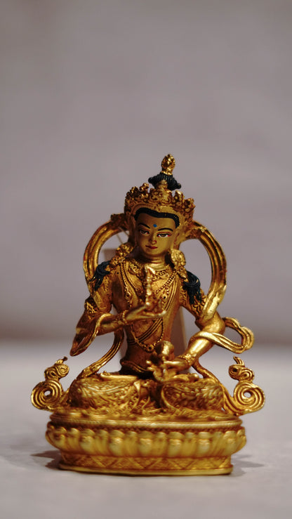 Golden statue of a seated Buddhist deity with intricate detailing, displayed on a plain background.