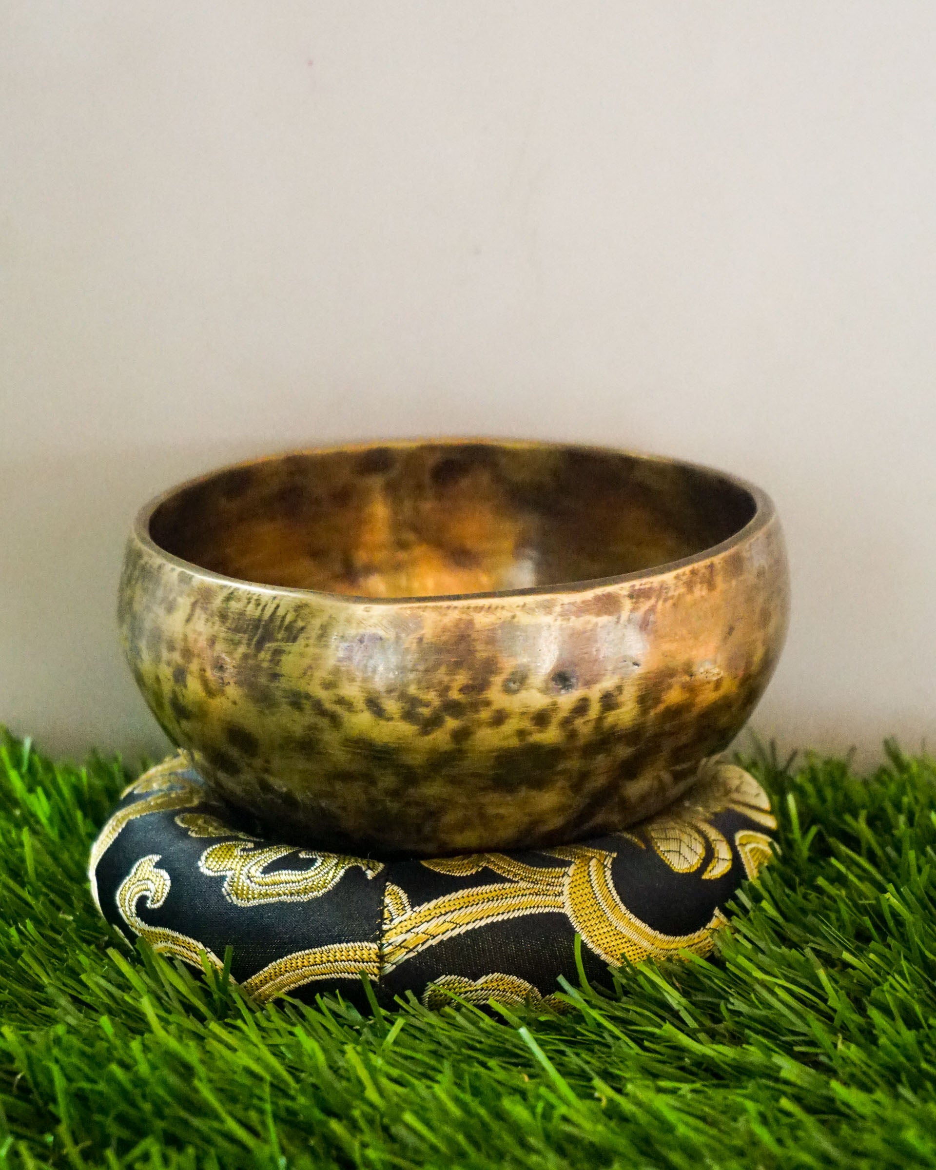 Brass singing bowl on a decorative pillow with a grassy background
