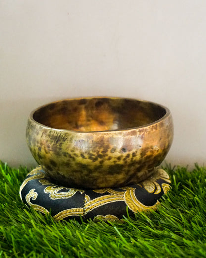 Brass singing bowl on a decorative pillow with a grassy background