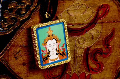 Square gold-framed Vajrasattva pendant with blue background, held in an open hand against a black backdrop.
