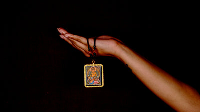Hand-painted Zambala miniature Thangka pendant in gold-accented copper Ghau locket displayed hanging from black beaded cord.