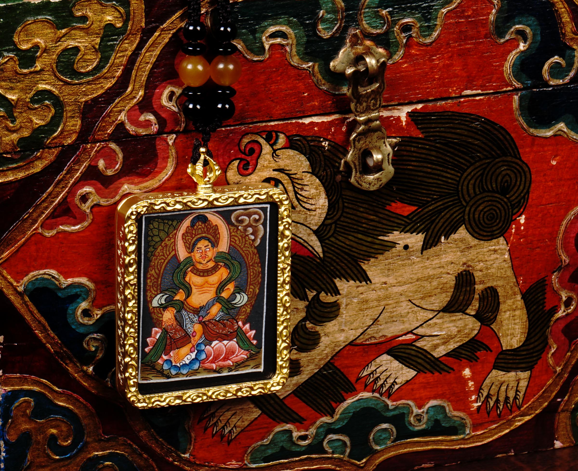 Hand-painted Zambala miniature Thangka pendant in gold-accented copper Ghau locket displayed hanging from black beaded cord.