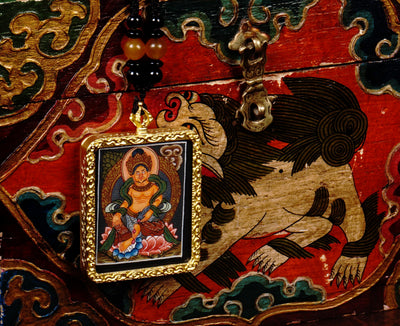 Hand-painted Zambala miniature Thangka pendant in gold-accented copper Ghau locket displayed hanging from black beaded cord.