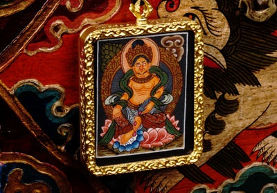 Hand-painted Zambala miniature Thangka pendant in gold-accented copper Ghau locket displayed hanging from black beaded cord.