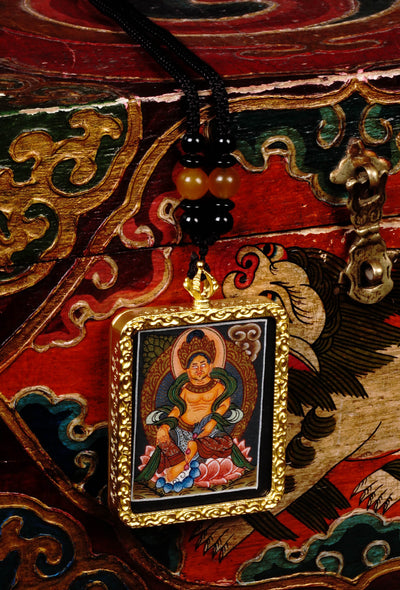 Hand-painted Zambala miniature Thangka pendant in gold-accented copper Ghau locket displayed hanging from black beaded cord.