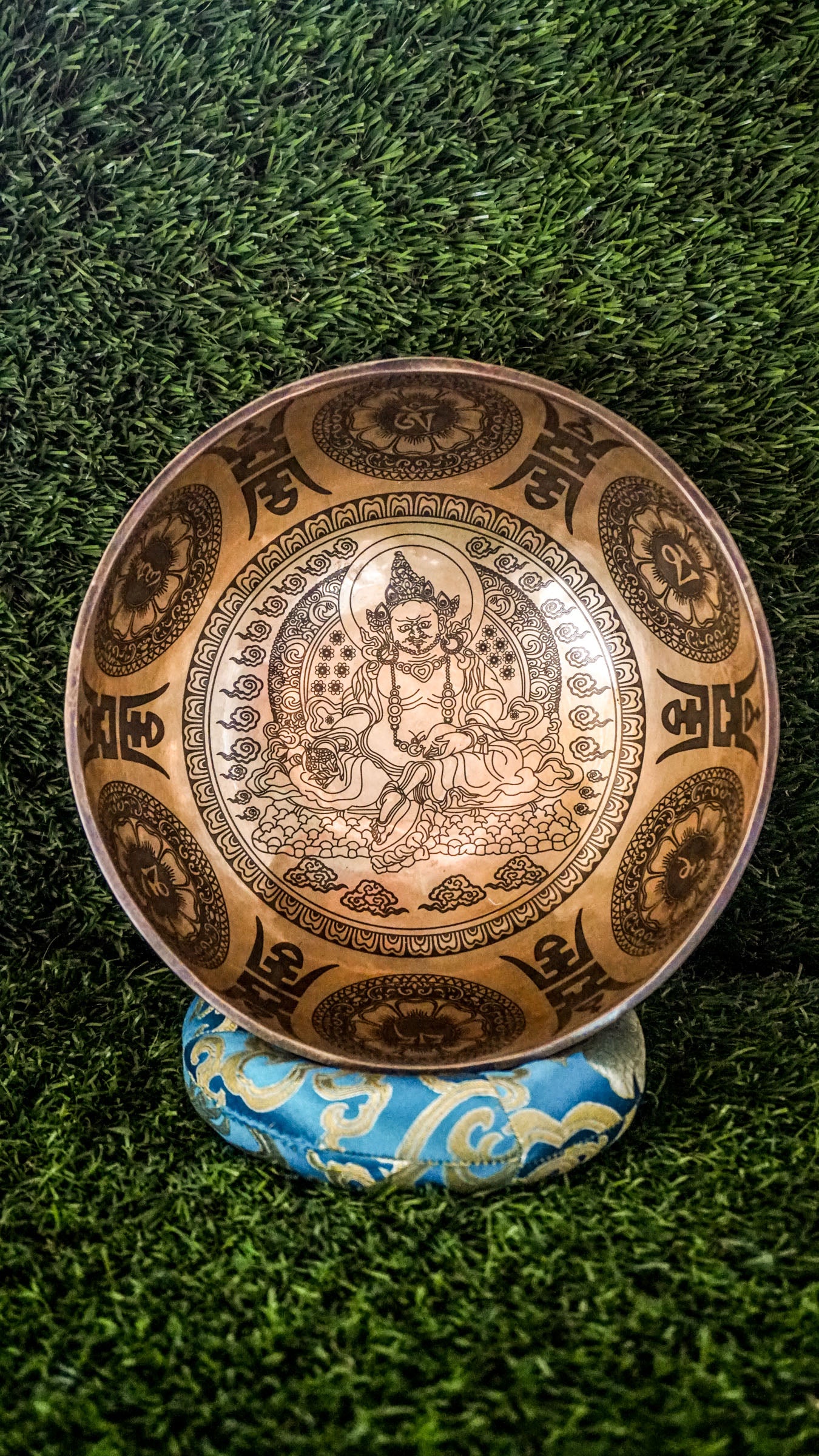 The Zambala Singing Bowl features Zambala, the deity of wealth and abundance, at its center with a radiant flower mandala. The outside is decorated with detailed mini mandalas and the Om Mani Padme Hum mantra, promoting prosperity and compassion. It produces rich, uplifting tones that support manifestation and spiritual grounding.