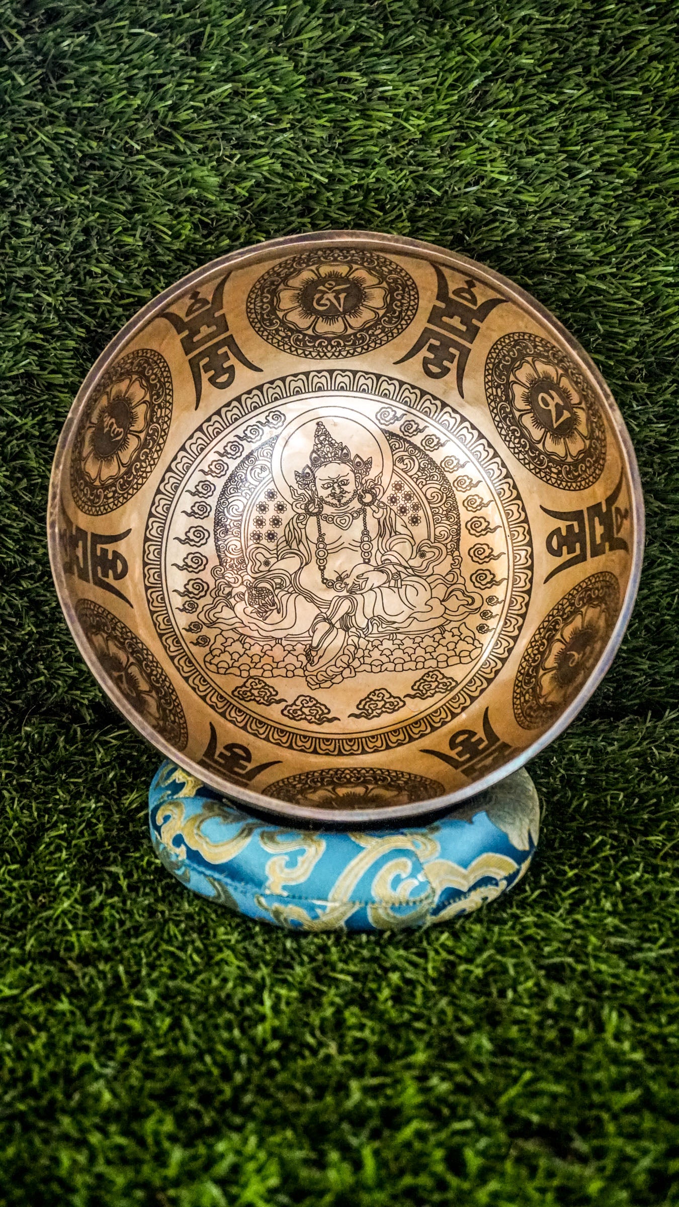 The Zambala Singing Bowl features Zambala, the deity of wealth and abundance, at its center with a radiant flower mandala. The outside is decorated with detailed mini mandalas and the Om Mani Padme Hum mantra, promoting prosperity and compassion. It produces rich, uplifting tones that support manifestation and spiritual grounding.