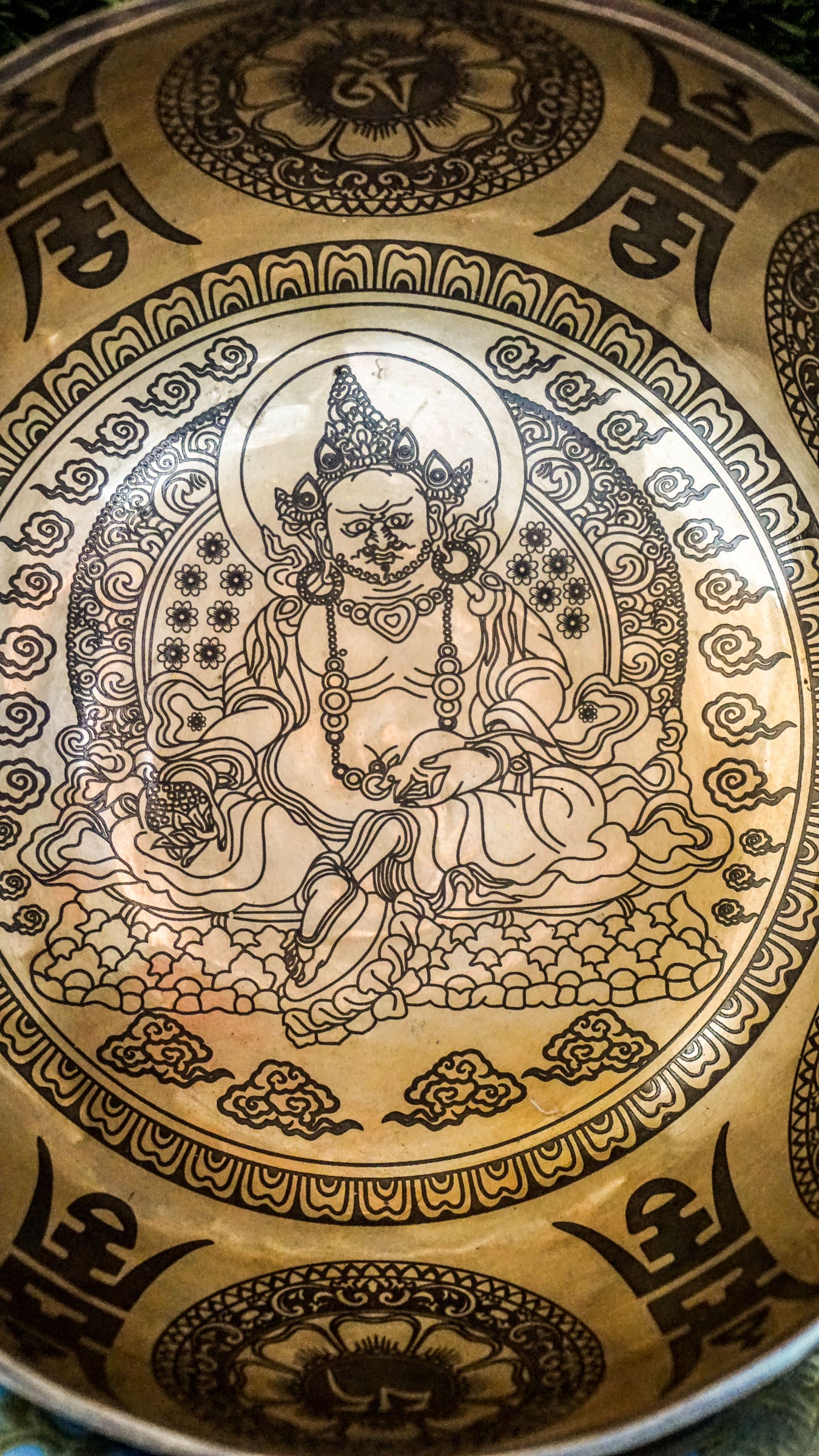 The Zambala Singing Bowl features Zambala, the deity of wealth and abundance, at its center with a radiant flower mandala. The outside is decorated with detailed mini mandalas and the Om Mani Padme Hum mantra, promoting prosperity and compassion. It produces rich, uplifting tones that support manifestation and spiritual grounding.