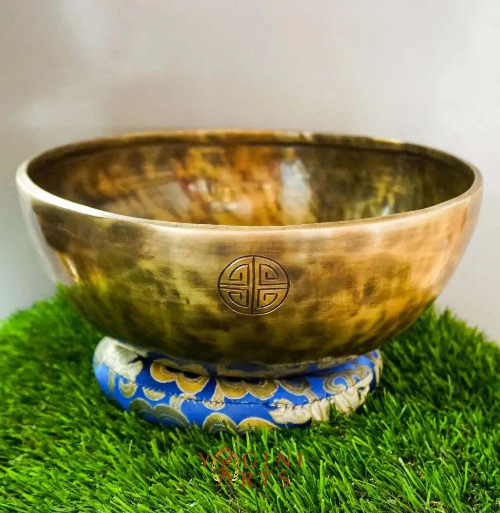 Bronze singing bowl with a decorative base on a grass-like surface