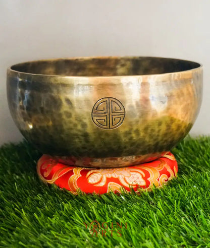 Bronze singing bowl with a red and gold base on grass