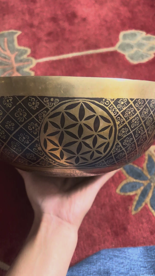 Load video: Golden Chengresi Tibetan singing bowl featuring sacred Buddhist engravings and geometric floral designs on a pink brocade cushion.