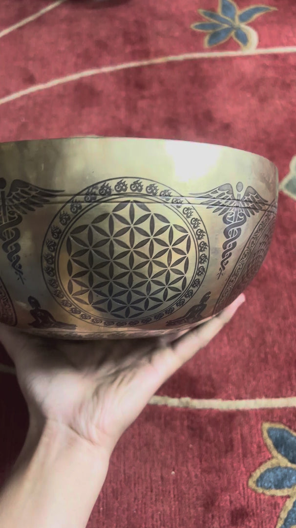Load video: Zambala engraved singing bowl shown upright with a wooden mallet and blue cushion, highlighting the intricate interior artwork.