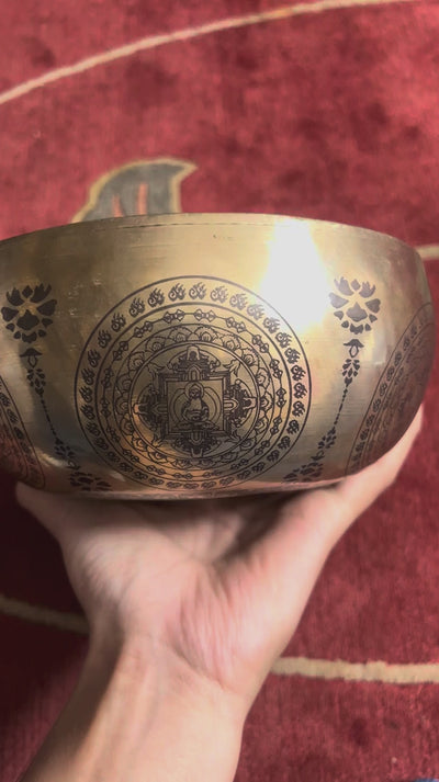 Green Tara singing bowl displayed upright with a wooden mallet, showing the central deity engraving and decorative circular patterns.