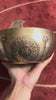 Green Tara singing bowl displayed upright with a wooden mallet, showing the central deity engraving and decorative circular patterns.