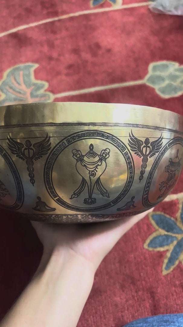 Golden Chakra Yogini singing bowl with engraved exterior motifs displayed on a purple brocade cushion