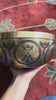 Golden Chakra Yogini singing bowl with engraved exterior motifs displayed on a purple brocade cushion