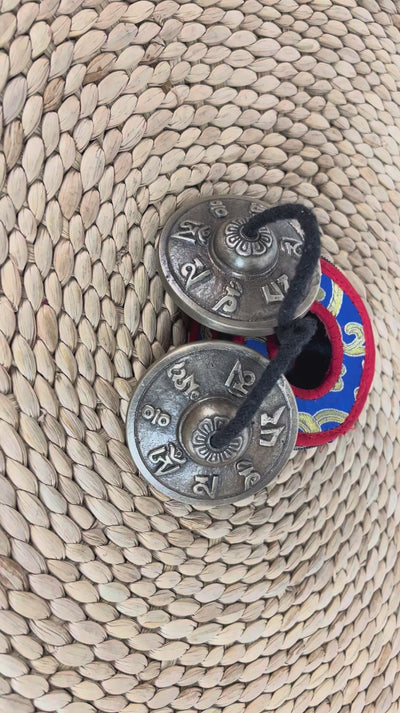 Close up of Tibetan Buddhist tingsha cymbals showing raised mantra symbols and detailed circular borders.