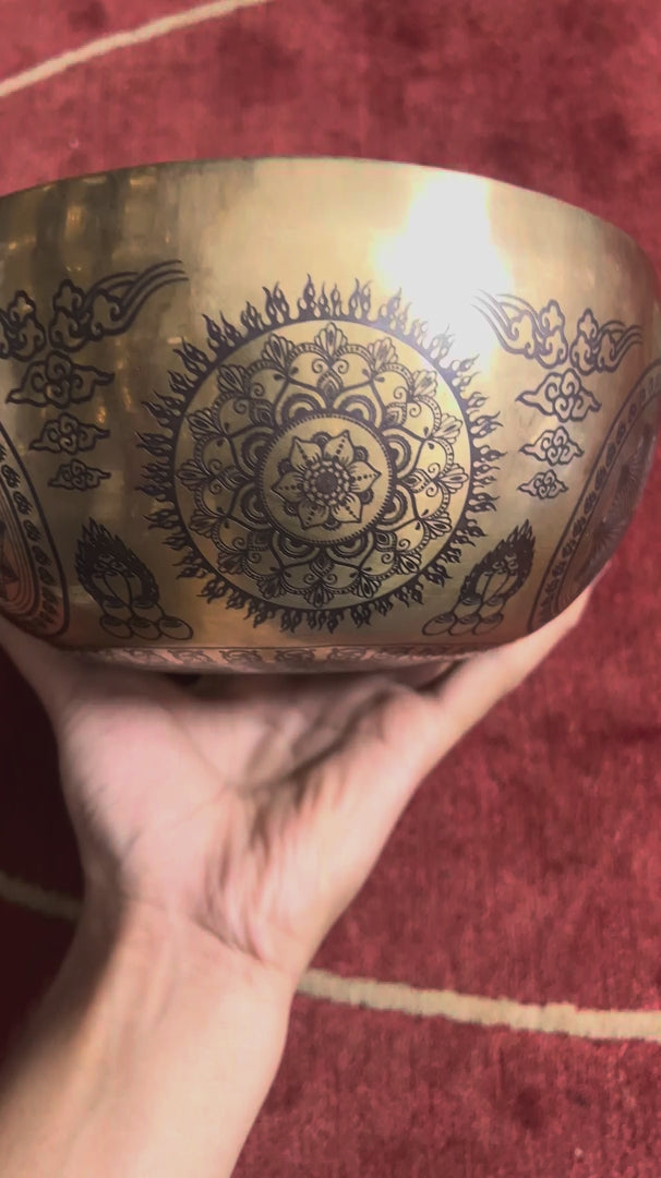 Load video: Floral Mandala singing bowl standing upright on a blue cushion beside a wooden mallet, showcasing its engraved interior design.
