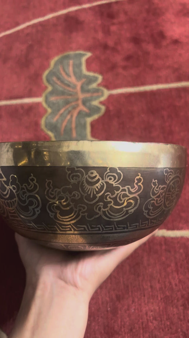 Tibetan singing bowl displaying the Flower of Life pattern inside, with a wooden mallet and blue brocade cushion.