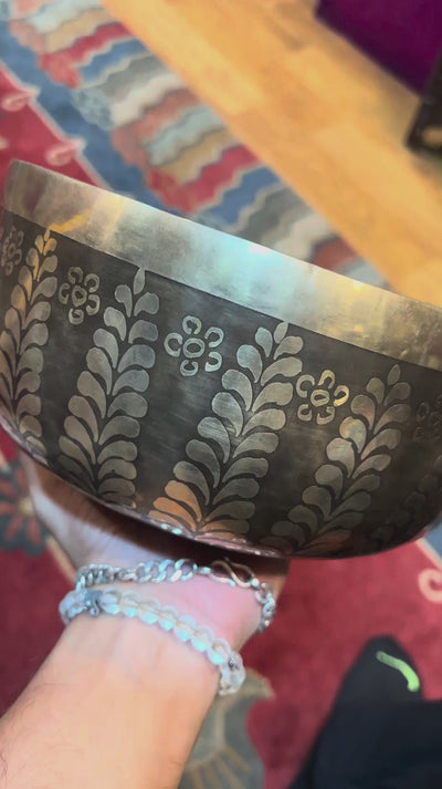 Handcrafted Nepal singing bowl with meditating figure and chakra engraving, floral design, bronze finish, cushion and wooden striker.