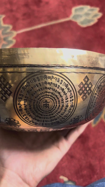 Close up of Medicine Buddha engraving surrounded by traditional Tibetan Buddhist symbols inside the singing bowl