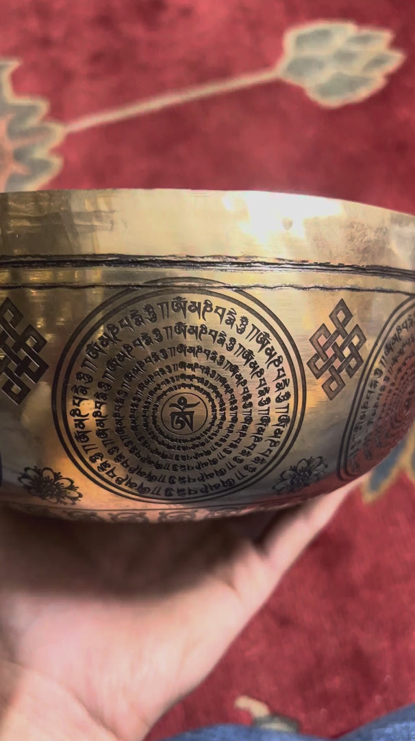 Close up of Medicine Buddha engraving surrounded by traditional Tibetan Buddhist symbols inside the singing bowl