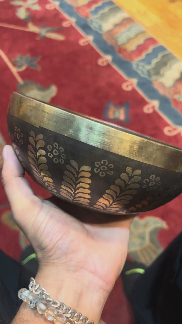 Handcrafted Yin Yang singing bowl from Nepal with gold floral engraving, dark bronze finish, decorative cushion and wooden striker.